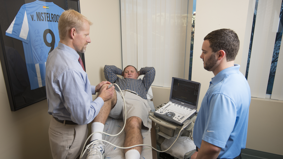 Physician showing at athletic trainer how to perform a knee ultrasound