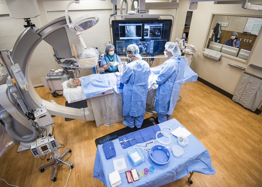 Multiple doctors stand around a patient and gesture to scans on a screen
