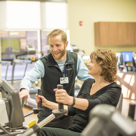 man assists woman with exercise machine