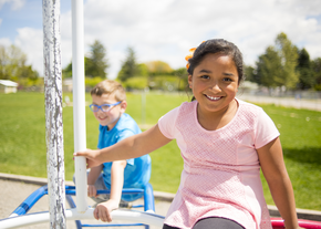 A child smiles at the camera while sitting on playground equipment