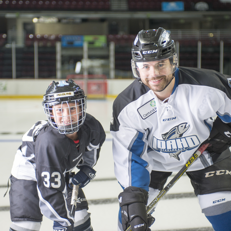 A hockey player with a little boy also dressed in hockey gear posing. 