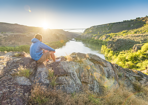 A man sits on a rock, looking at a river