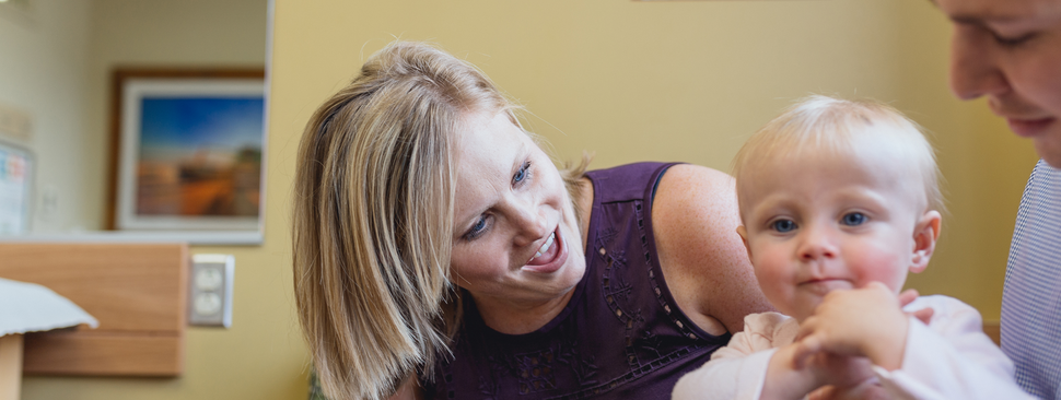 Mother and father play with child in hospital room.