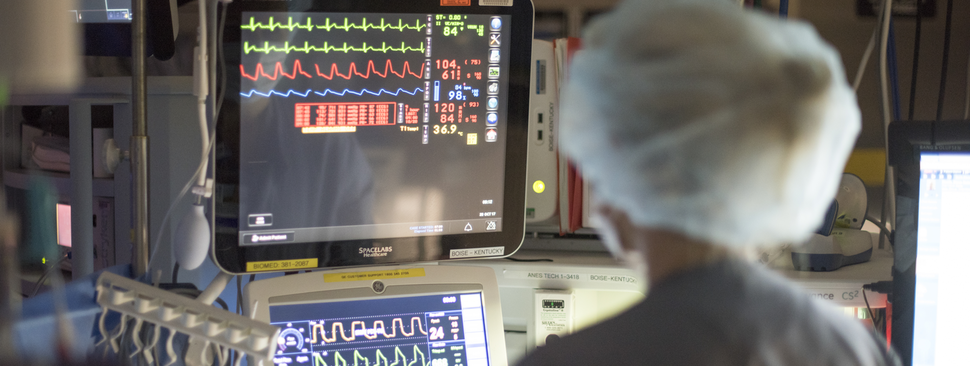 A medical professional watches screens in a surgery room