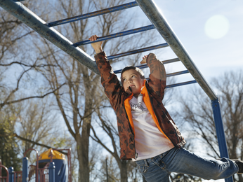 Boy swings on monkey bars outdoors.