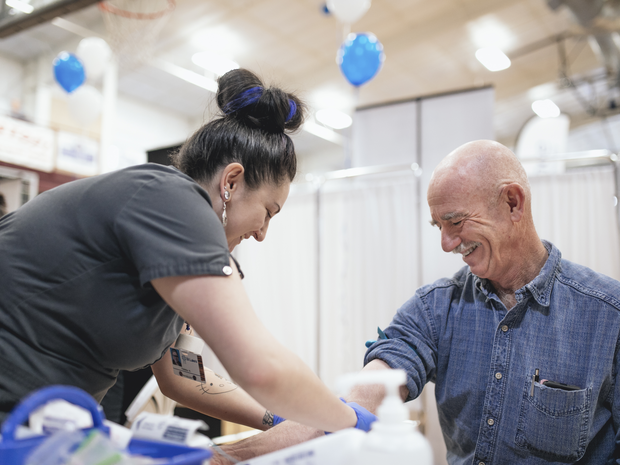 Man smiles while getting blood pressure drawn at health event.