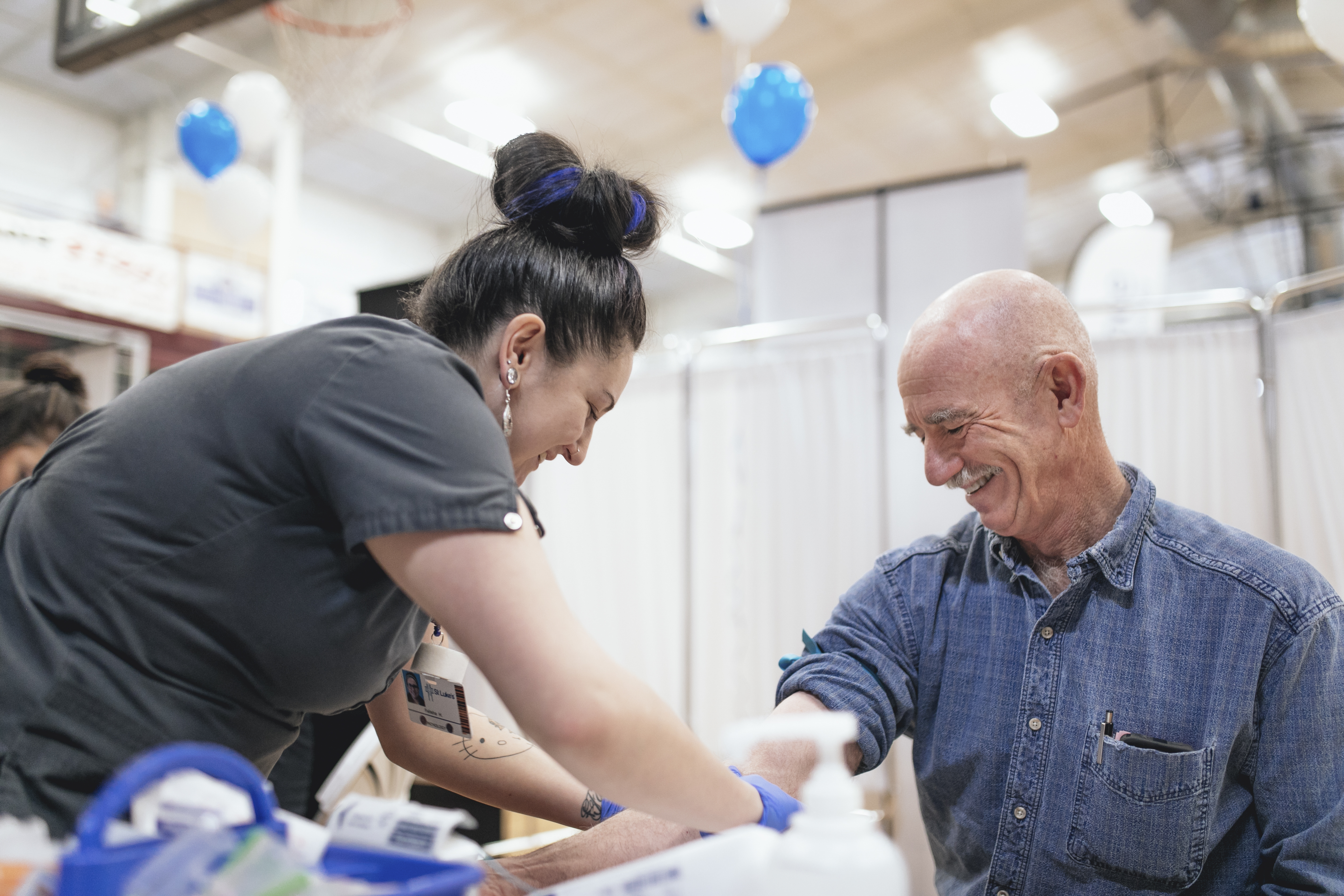 Man smiles while getting blood drawn at health screening event.