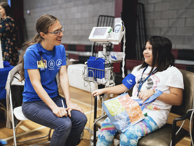 Volunteer sits with young patient getting her blood pressure taken.