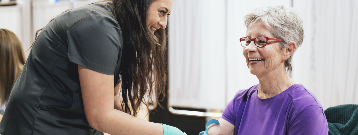 Woman smiles while getting her blood drawn at health event.