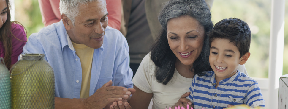 Young boy blows out birthday candles with grandparents