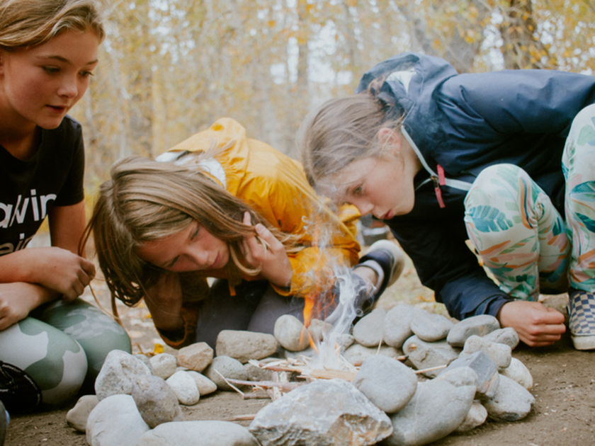  Three girls work on starting a fire.