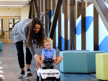 Young patient being pushed in toy car through sky bridge