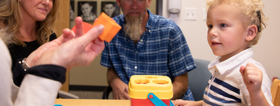 A boy with a hearing aid playing with blocks with a nurse
