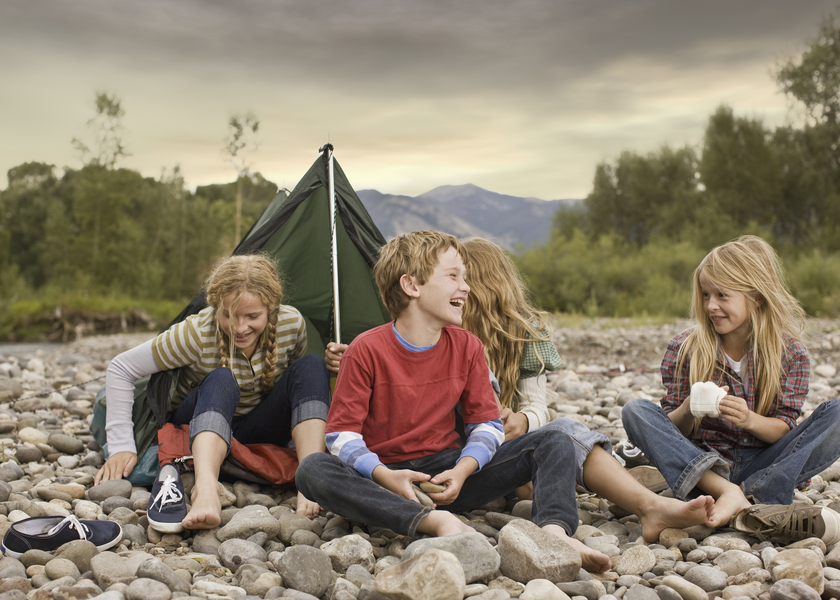 A group of kids laugh outside of a tent in a field