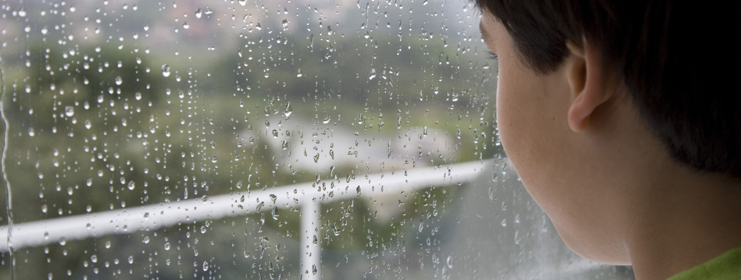 A boy looks out of a rainy window