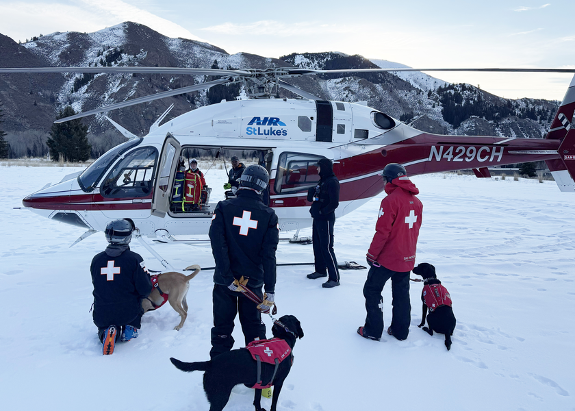 Group of dogs and handlers gather around the helicopter. 