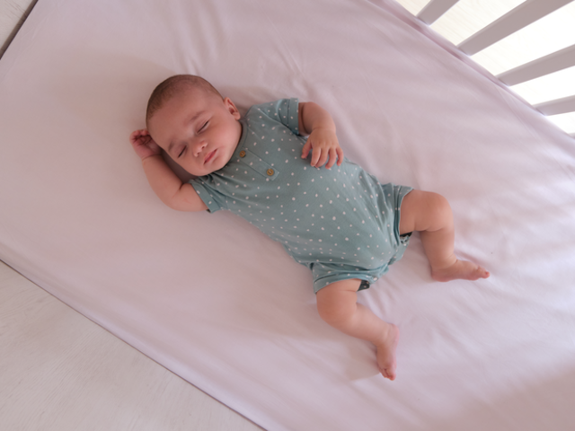 Baby lying in crib with lavender sheets.