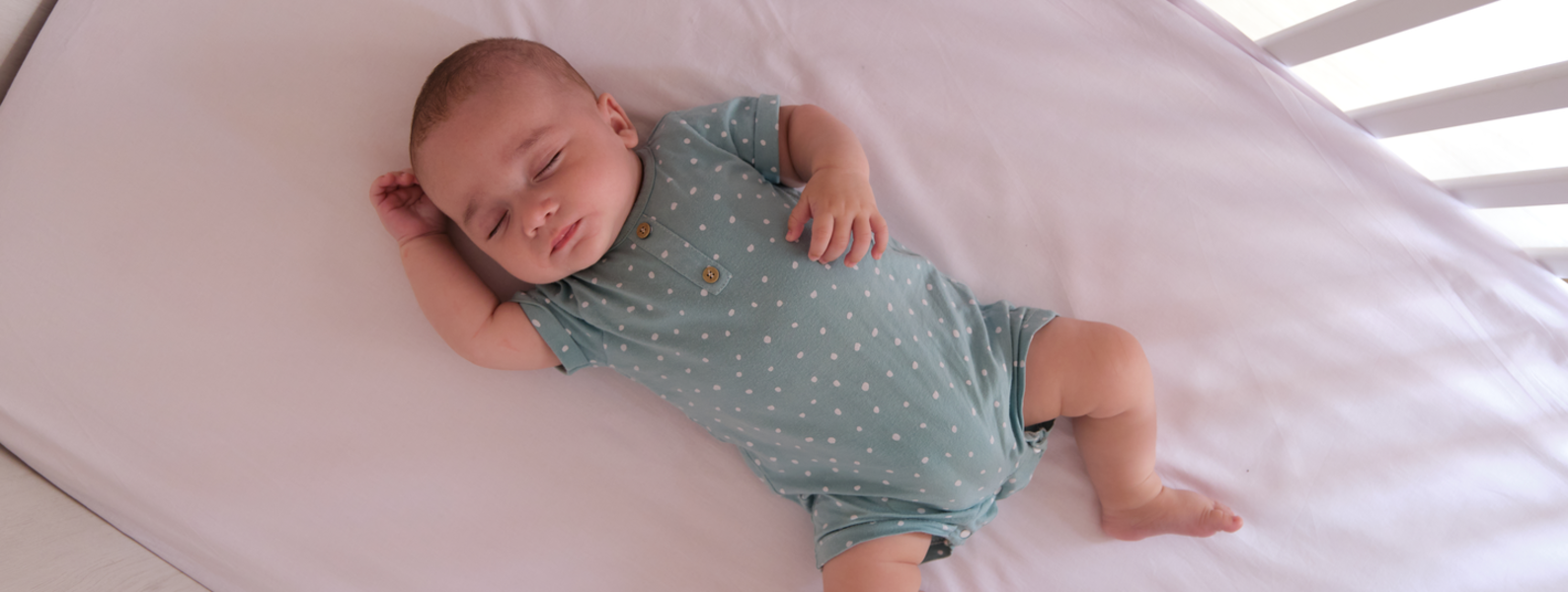 Baby lying in crib with lavender sheets.