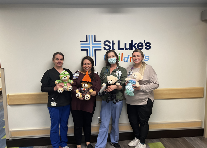 Women hold teddy bears in front of St. Luke's Children's sign