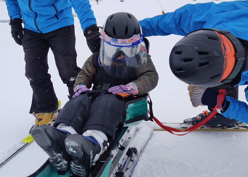  Child using adaptive ski equipment on the mountain with two adults instructors.