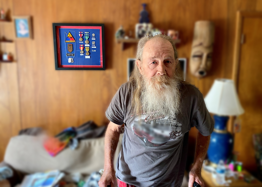Doc standing in his living room in front of a display of his medals.