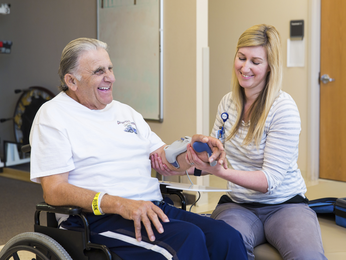 Man in wheelchair smiles while provider works on his arm.