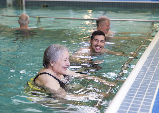 Man and woman smile in pool during rehabilitation class.