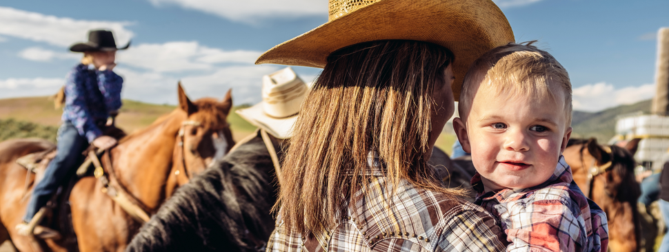 Toddler being held by his mom while they are working on the ranch.