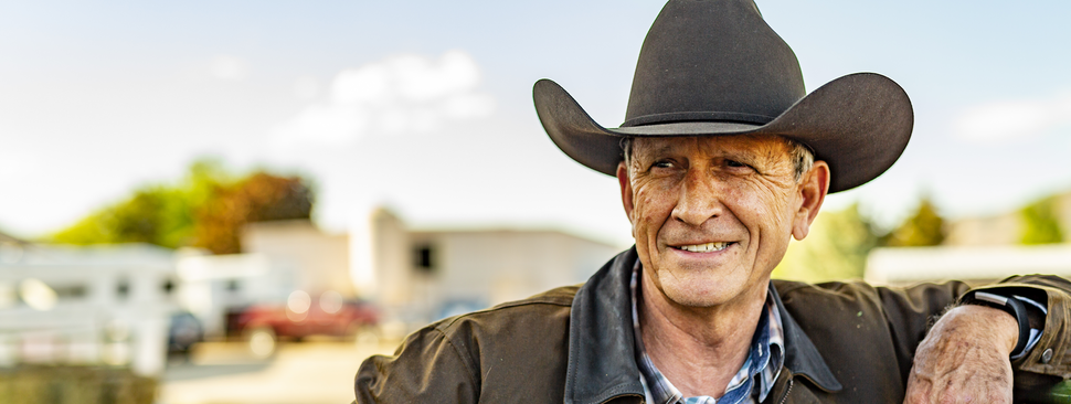A man in a cowboy hat leans on a gate