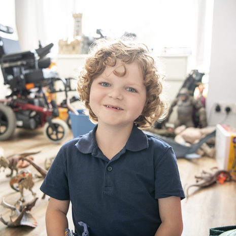 Cheerful boy with muscular dystrophy sitting on playroom floor surrounded by dinosaur toys