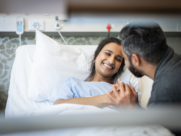 Patient smiles on hospital bed while embracing partner.