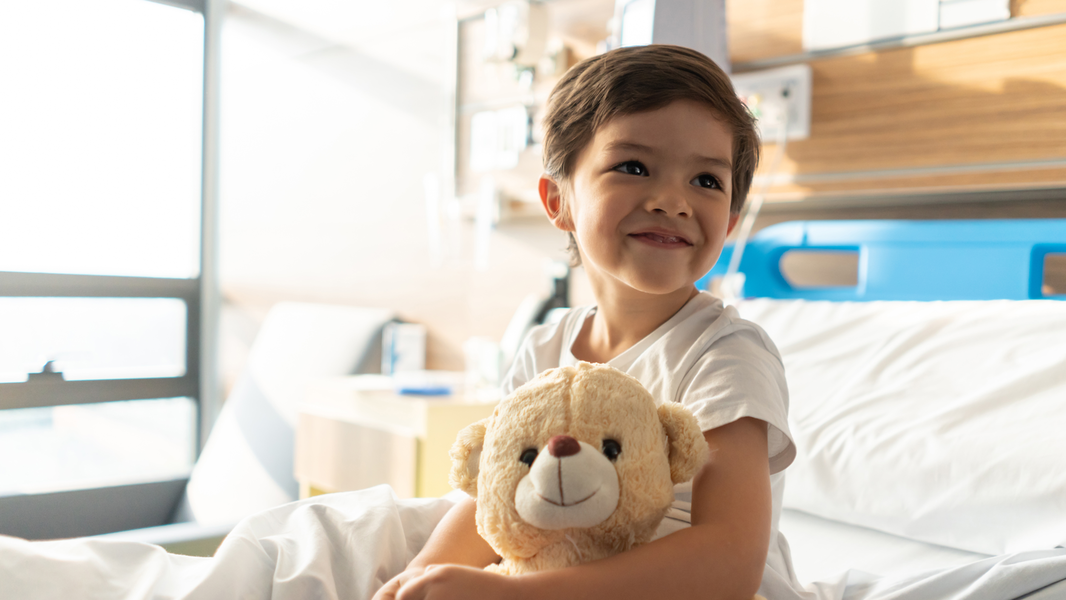 Child in hospital bed holds teddy bear