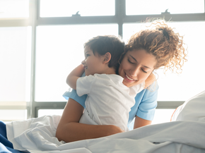 Child on hospital bed hugs caregiver