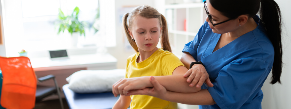 A nurse helps a young girl with her elbow.
