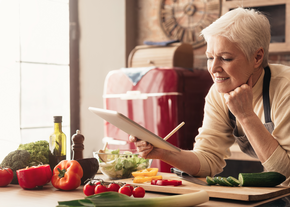 A woman leans over the counter, holding a tablet in one hand