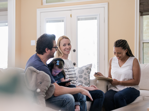 Young family speaks with smiling researcher at their home.