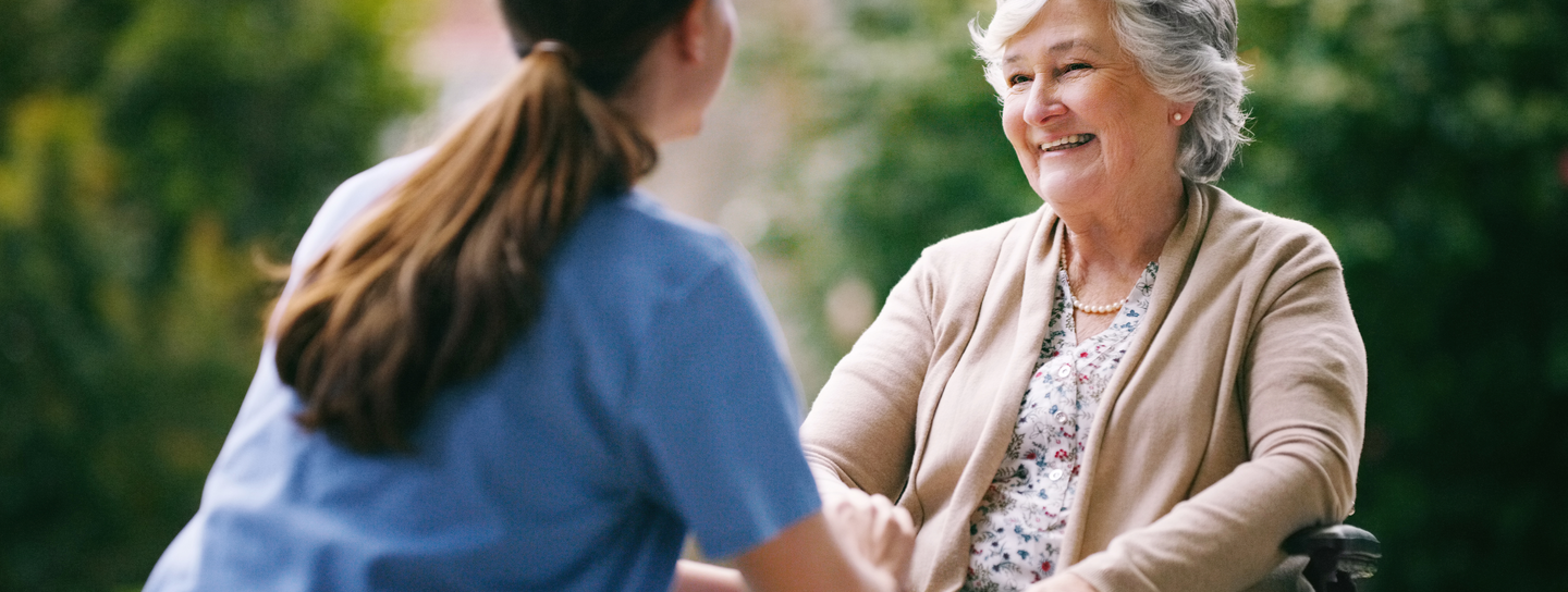 A woman in a wheelchair smiles at a nurse who is seated in front of her