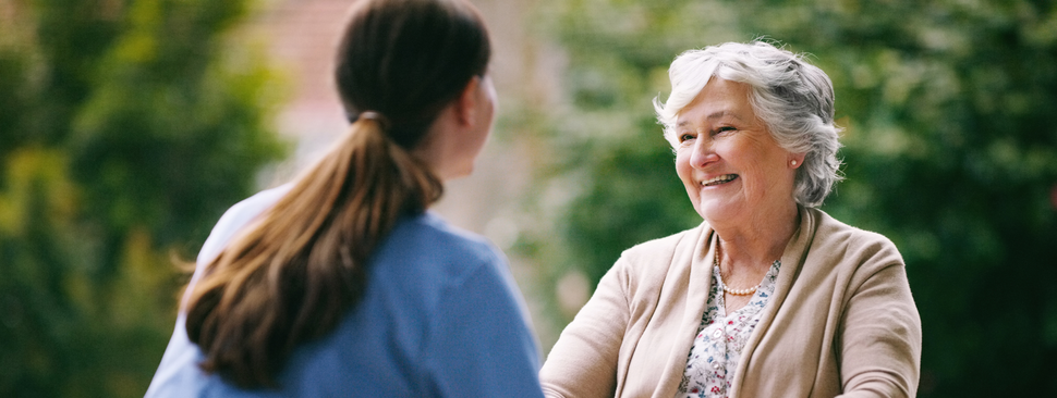 A woman in a wheelchair smiles at a nurse who is seated in front of her