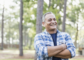 A man in a plaid shirt smiles with his arms crossed