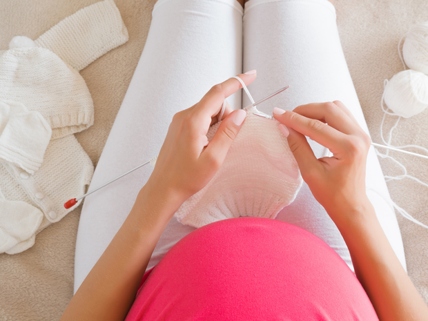 Pregnant woman sitting on bed knitting