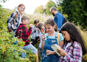 Children observe greenery outdoors while being supervised by two adults