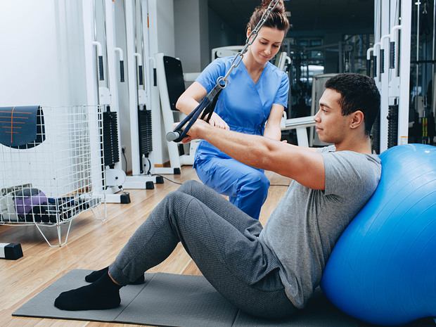 A male patient working with a nurse against a yoga ball