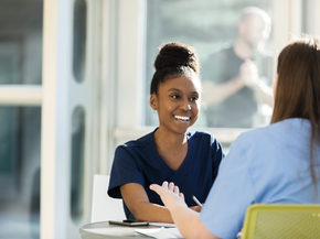 Women speaking to one another at a table.