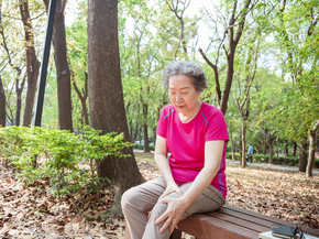 Woman sitting on a park bench holding her knee