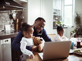 Man on phone with laptop open and family close by.