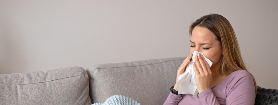 woman sits on the couch blowing her nose
