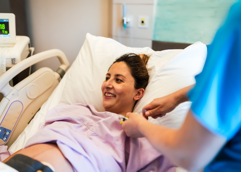 A pregnant woman smiles as she lays in a hospital bed