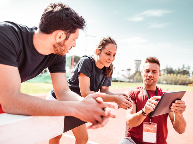 Trainer with tablet provides instruction to athletes on track.