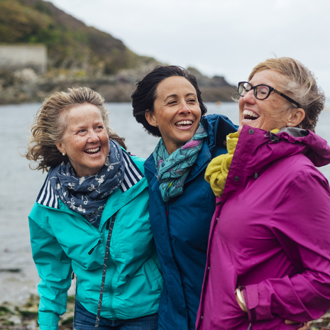 Friends exploring the outdoors together, standing with their arms around each other at the coast.