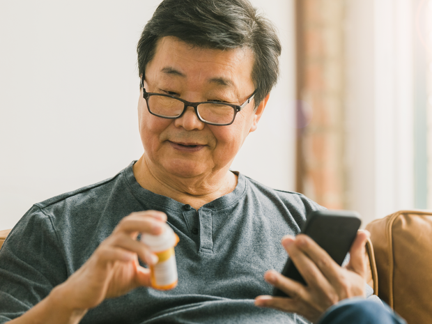 Senior man looking at a prescription bottle and holding a cell phone